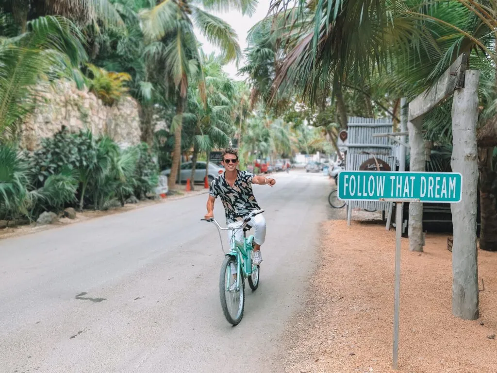 A person riding a bicycle next to a sign that says "follow your dreams."