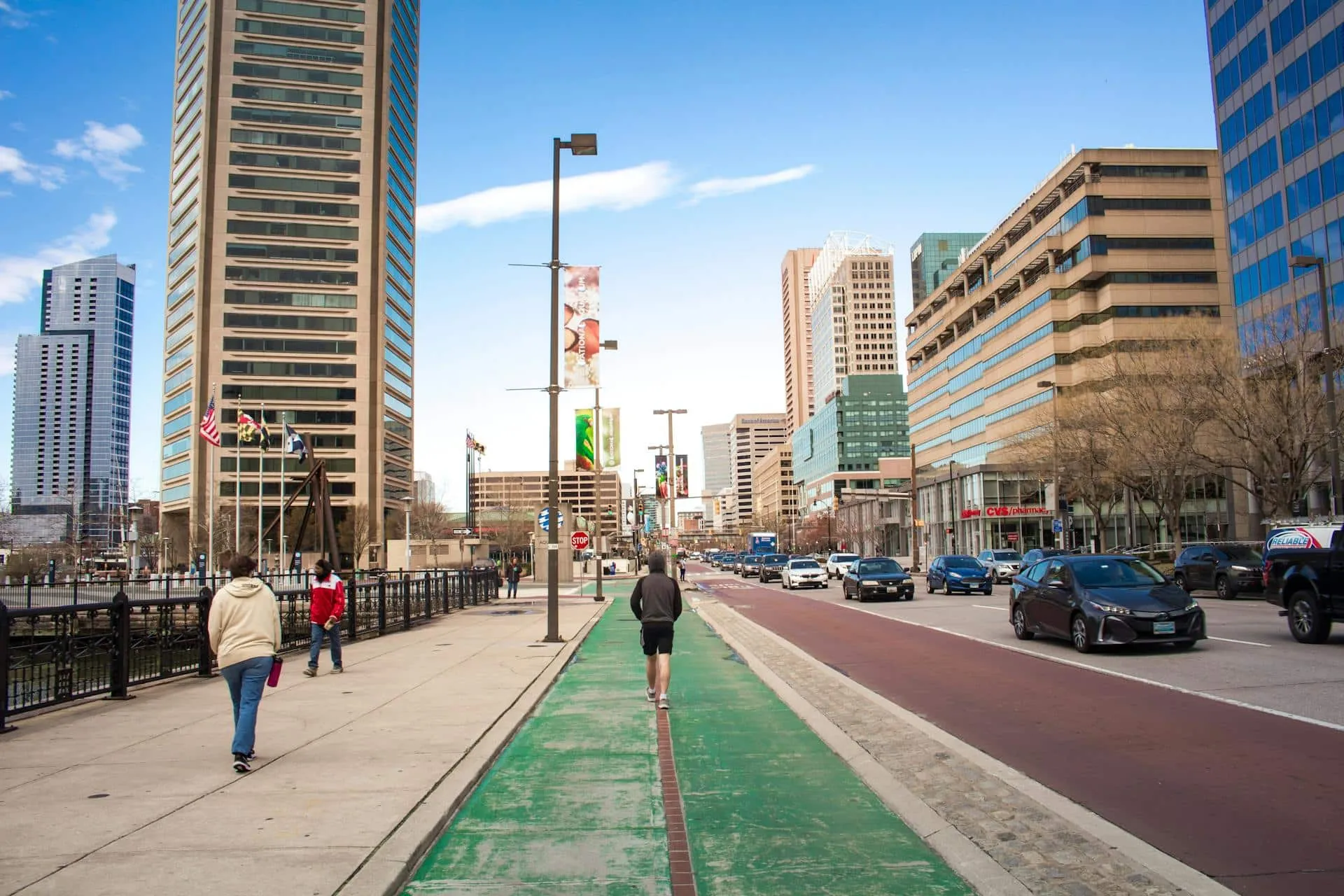 People walking on the roadside near moving cars and concrete buildings.