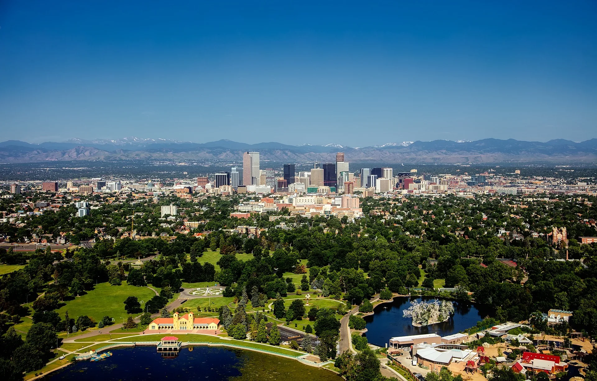 Aerial view of Denver, Colorado, showcasing the city's skyline with green parks and the Rocky Mountains in the background.