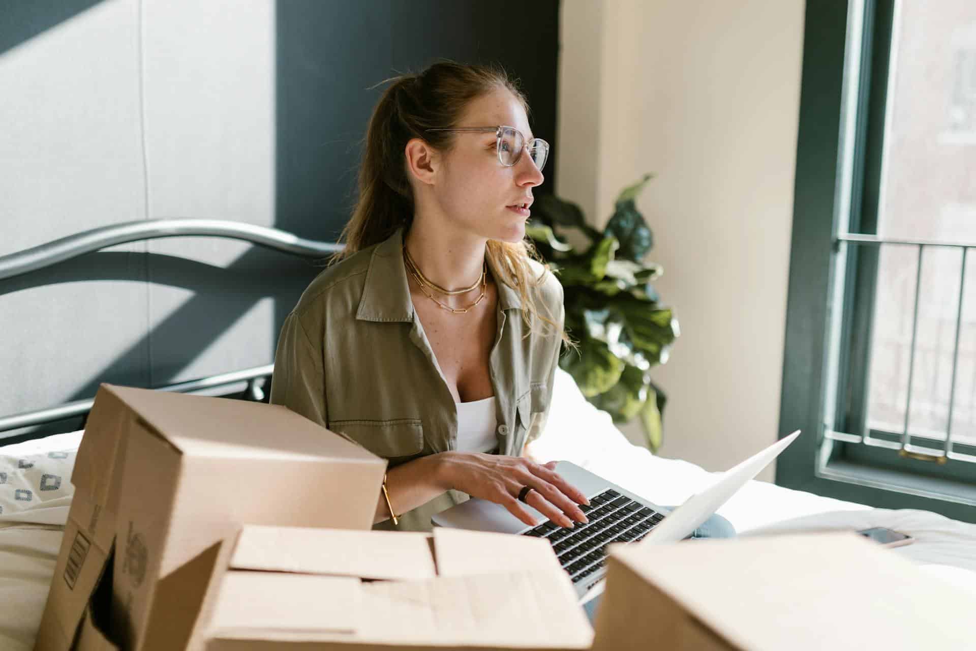 A woman working on a laptop surrounded by moving boxes.