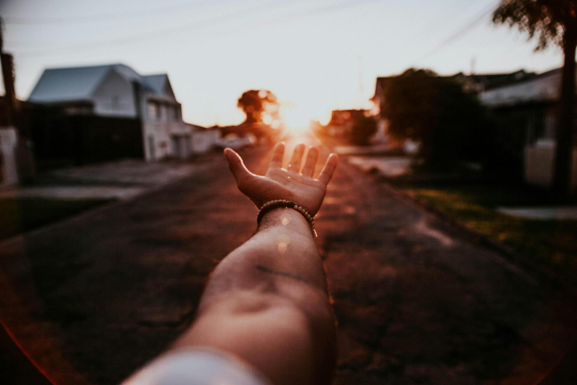 Outstretched hand reaching toward a beautiful sunset over a quiet suburban street, symbolizing new beginnings.