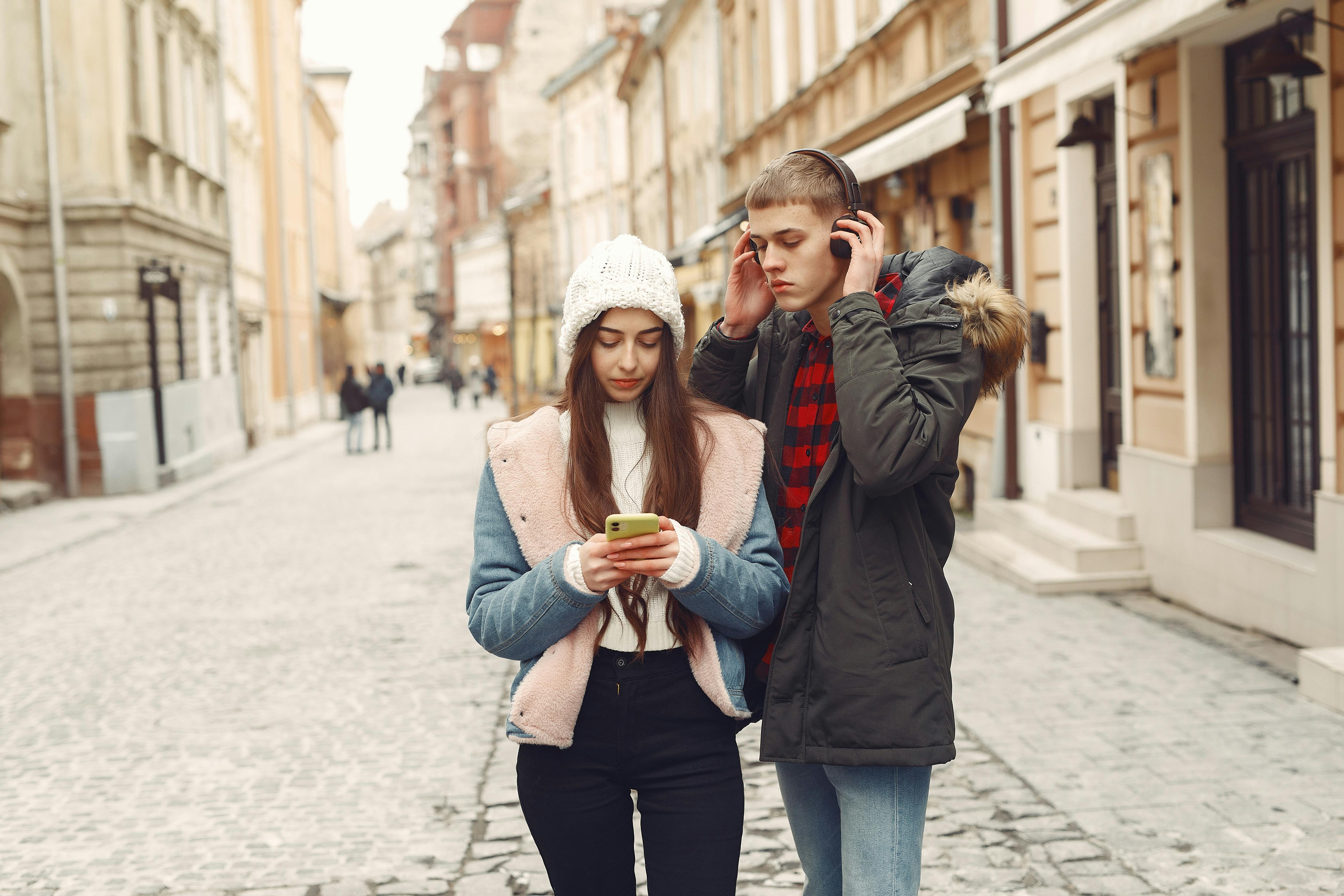 A young man and woman dressed in winter clothes walk along a cobblestone street.