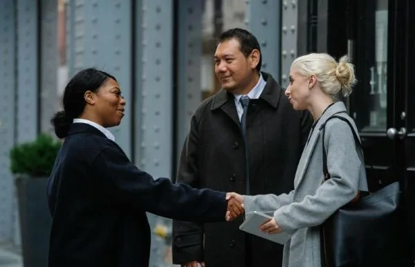 three professionally dressed individuals engaged in a handshake outdoors, suggesting a business or formal meeting